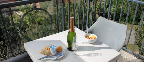 A balcony with a table set for a meal, including croissants, a bottle of champagne, and a bowl of fruit.