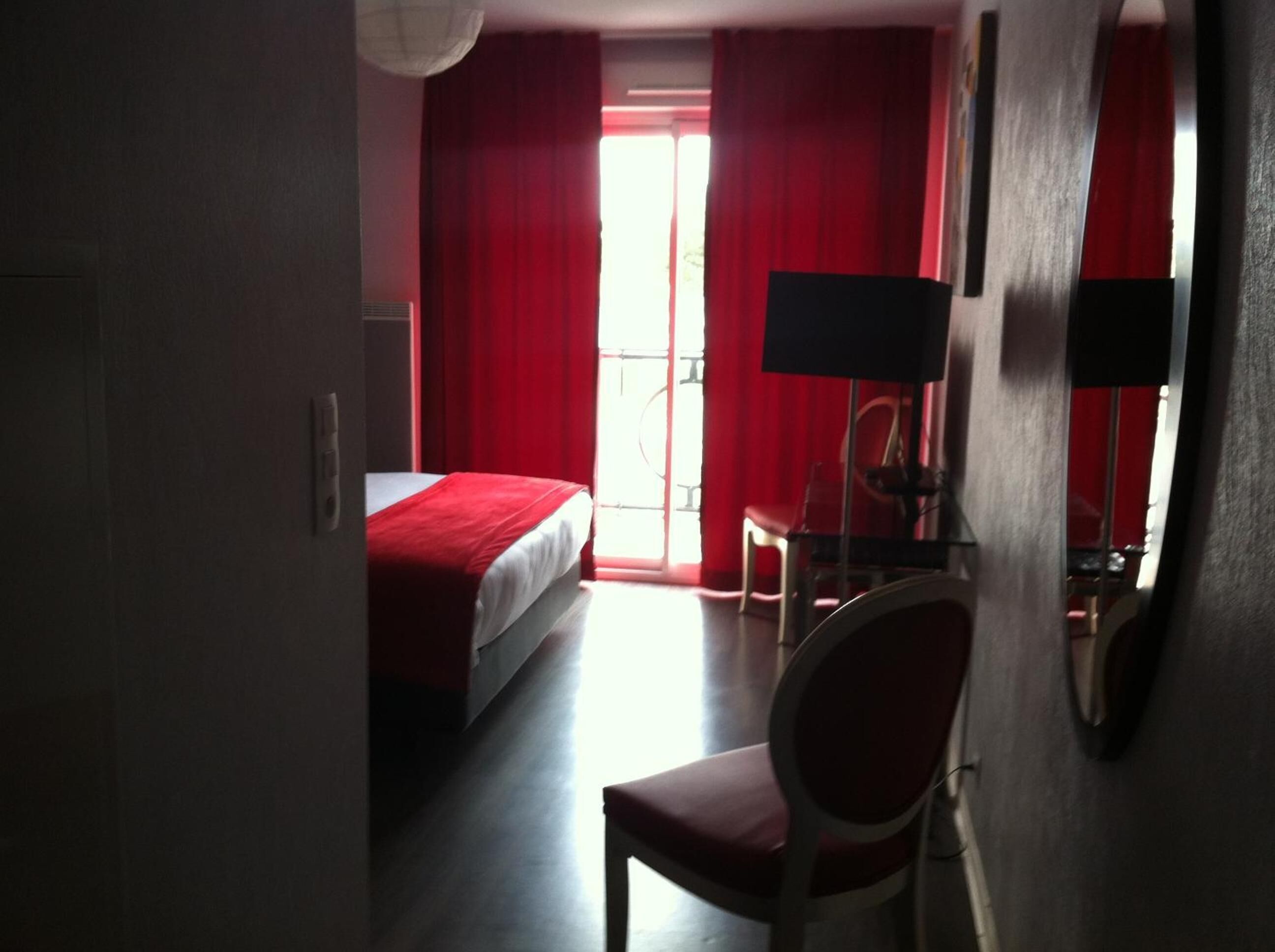Ein Hotelzimmer mit einem Bett, einem Schreibtisch mit Stuhl und einem großen Fenster mit roten Vorhängen.