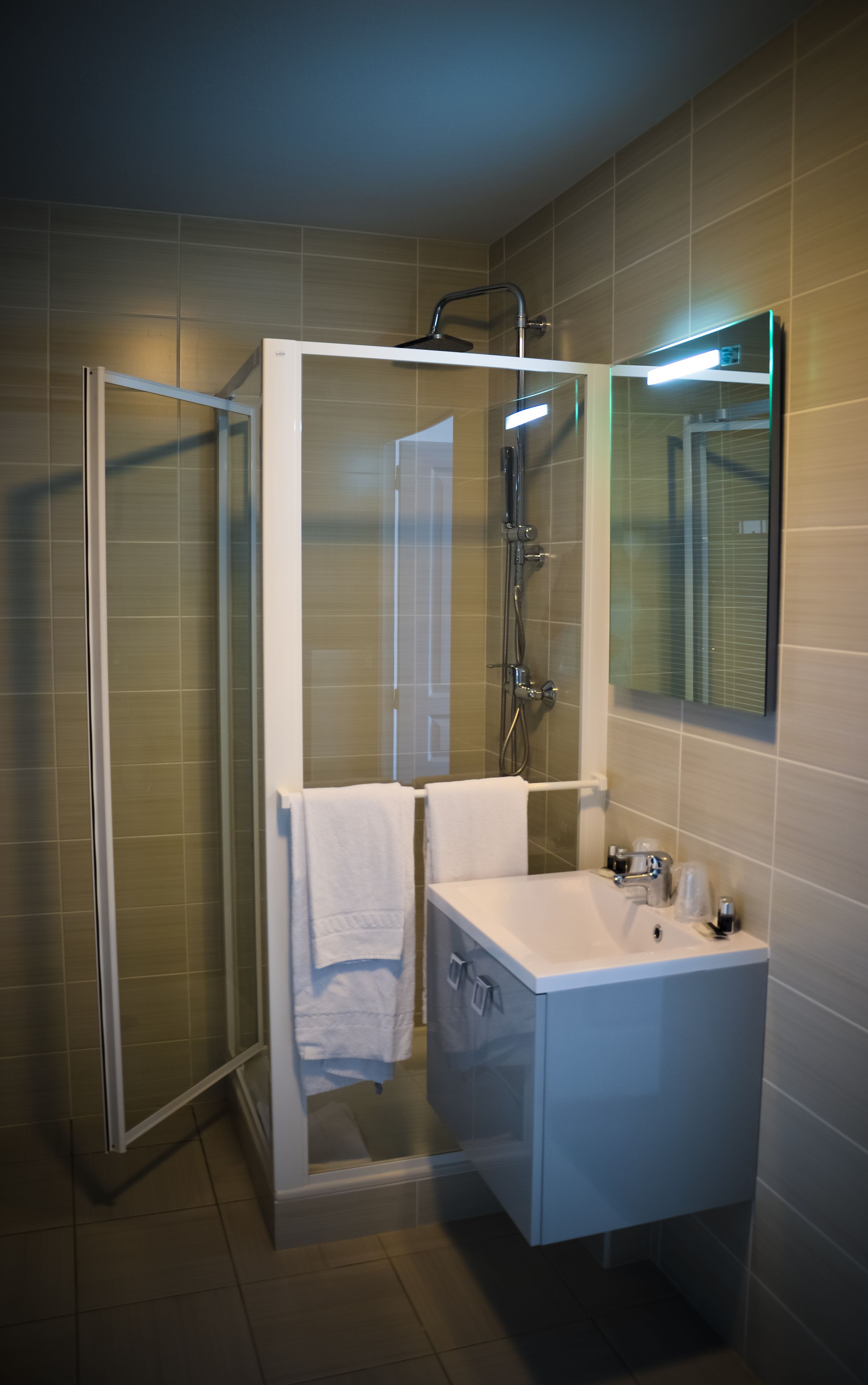 Ett modernt badrum med en dusch som är avskärmad med glasväggar, ett vitt handfat och en spegel ovanför.