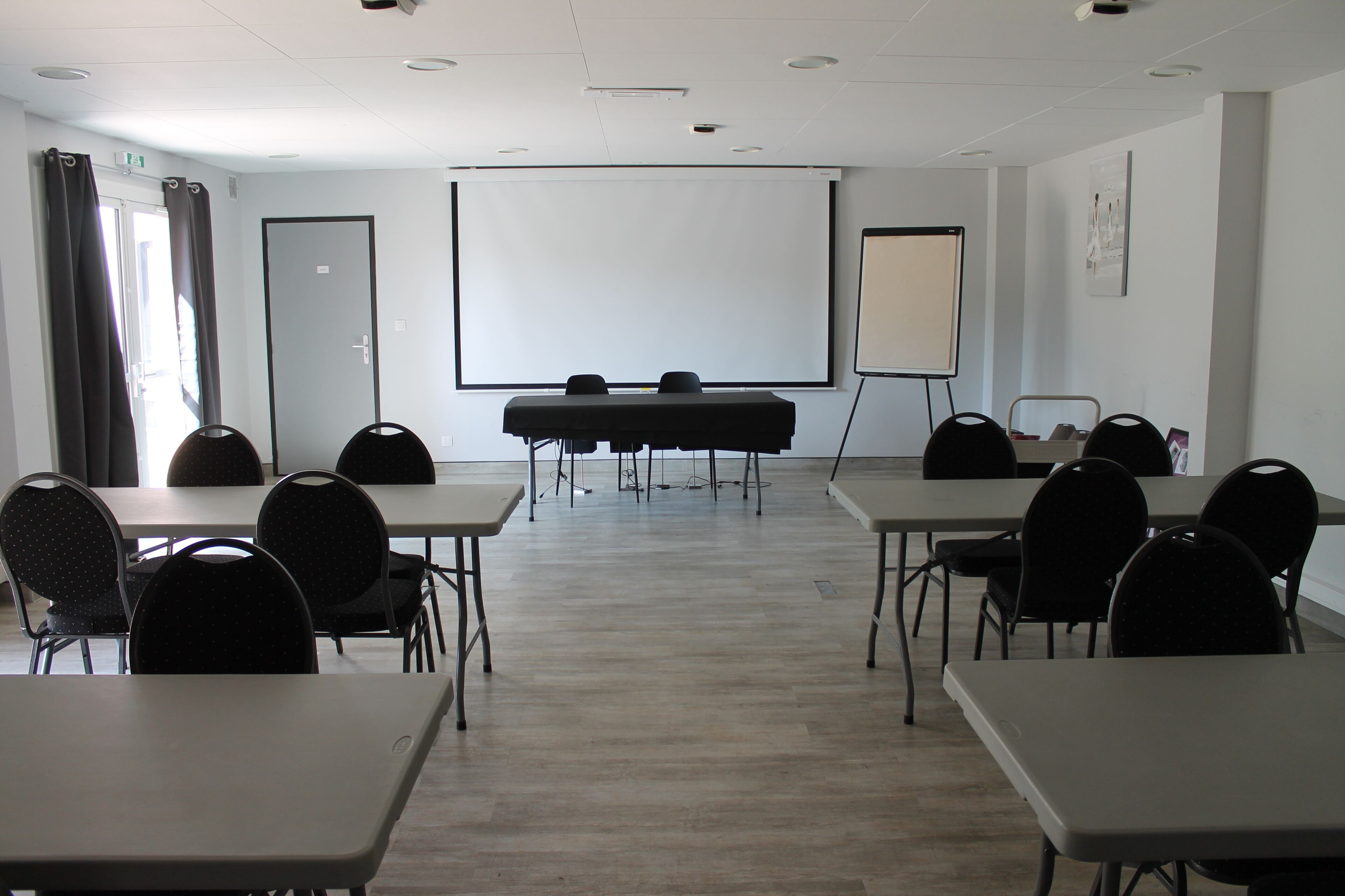 Een vergaderruimte met tafels, stoelen, een projectiescherm en een whiteboard.