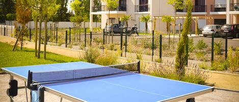 Une table de ping-pong installée à l’extérieur, dans un quartier résidentiel, avec des immeubles d’habitation en arrière-plan.