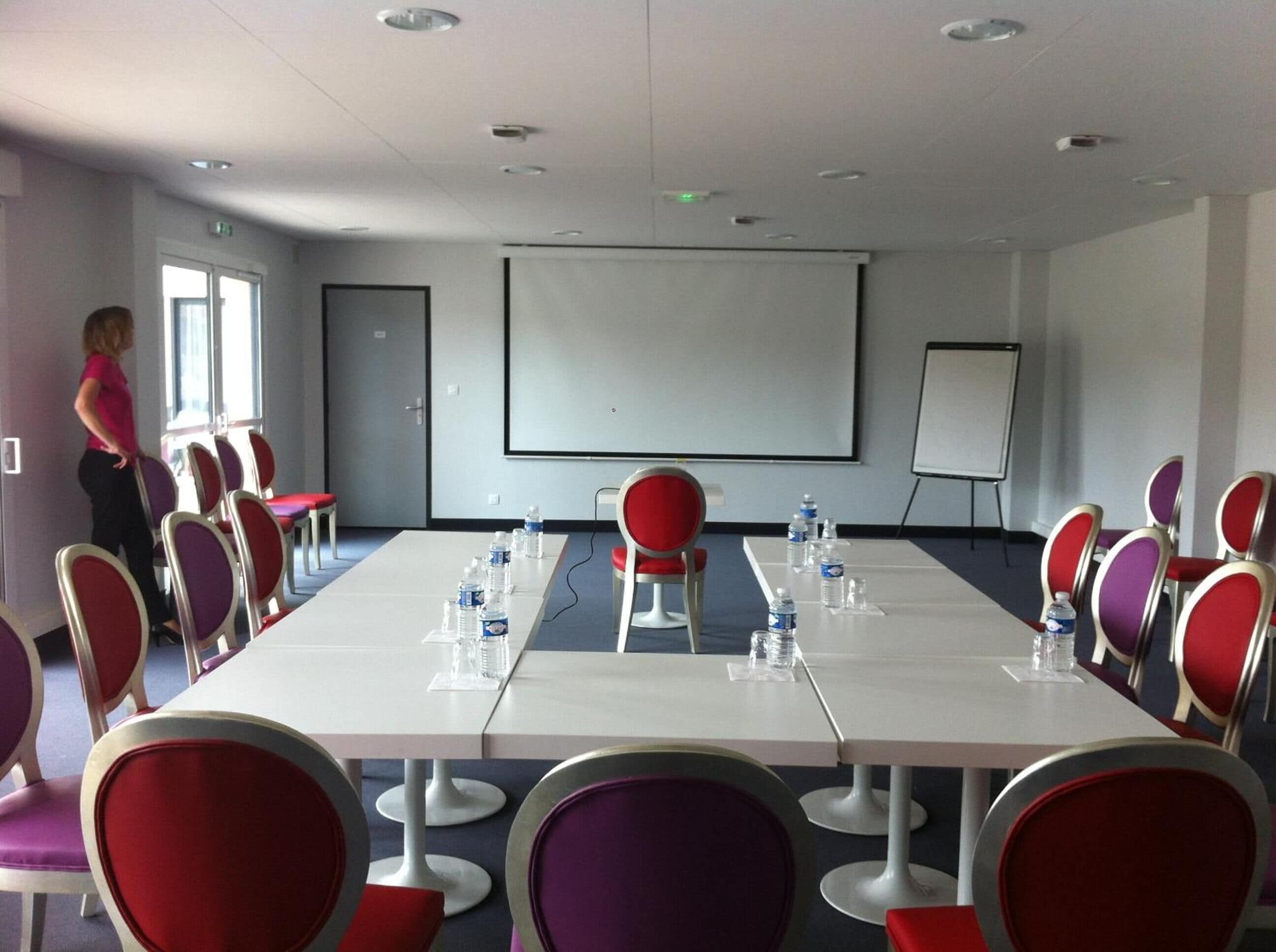 A conference room with a long table, chairs, a projector screen, and water bottles.