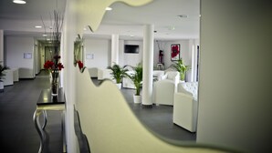 A modern waiting area with white furniture, a reception desk, and potted plants. - Adonis La Baule (La Baule-Escoublac)