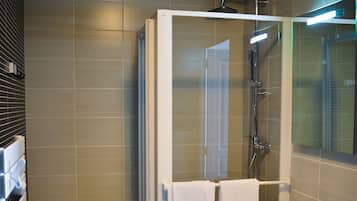 Een moderne badkamer met een douchecabine van glas, een wit wastafeltje en een handdoekrek.