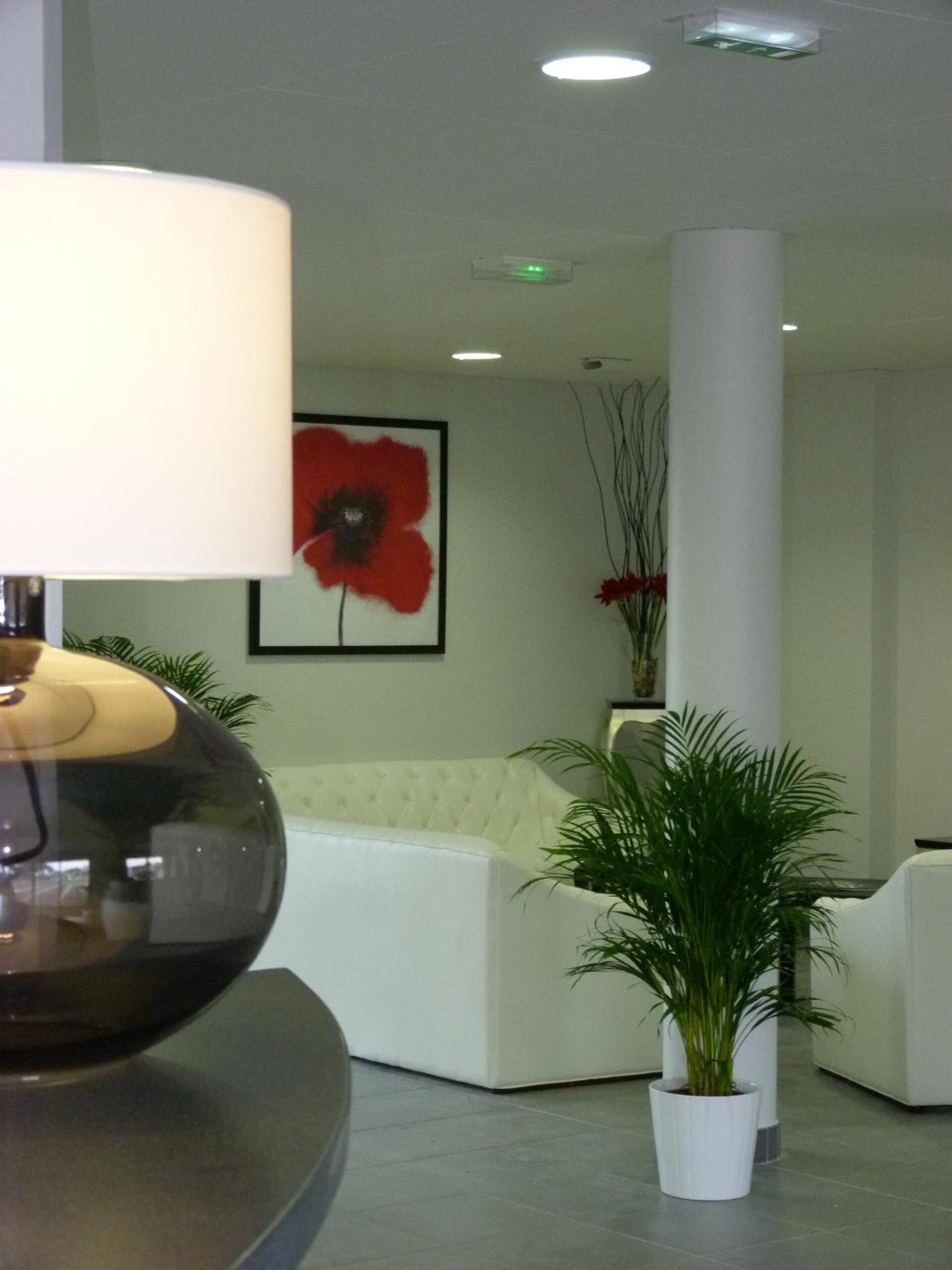 A modern lobby with a round table, a white sofa, a potted plant, and a red flower painting on the wall.