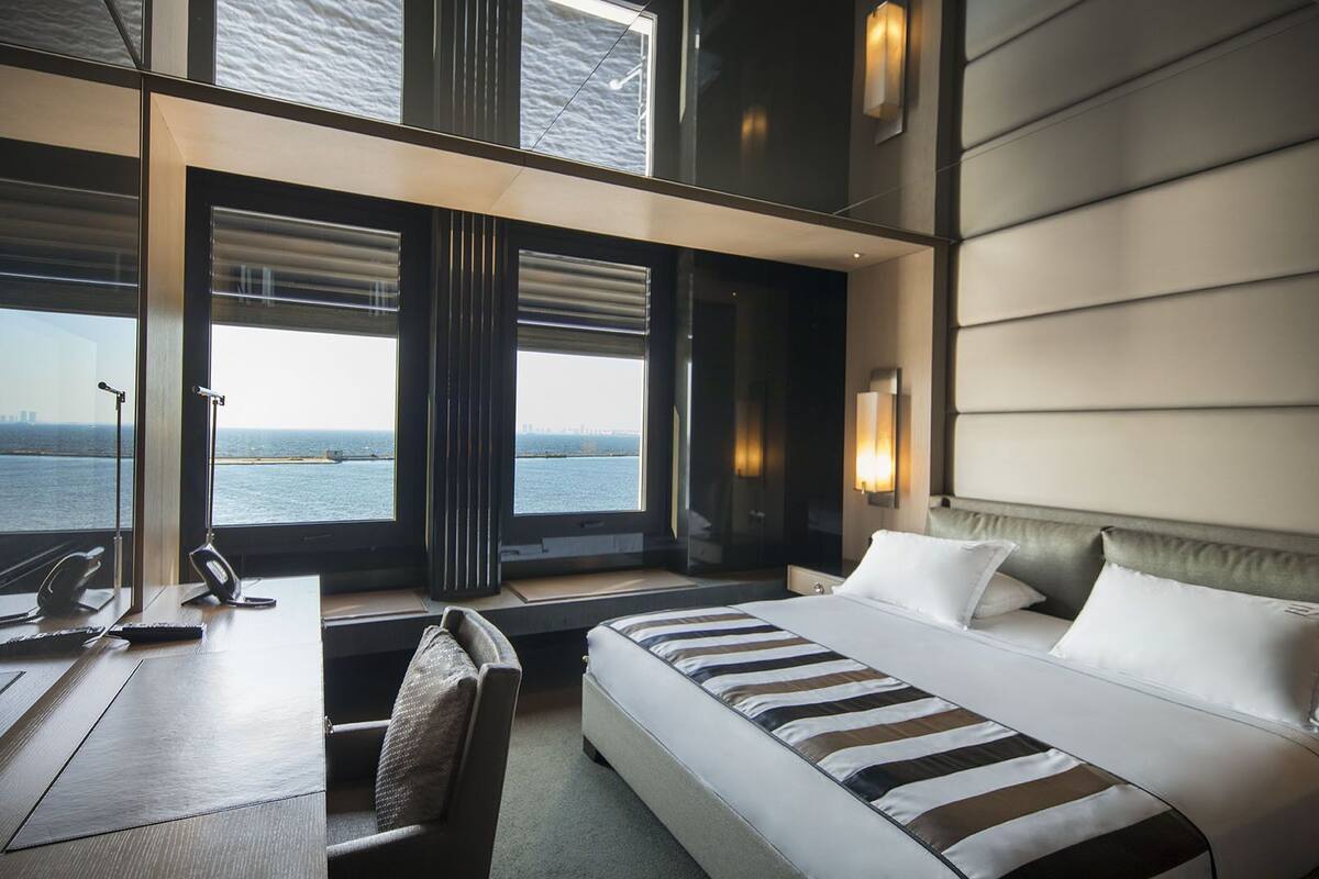 A hotel room with a large bed, a desk, and a view of the sea.