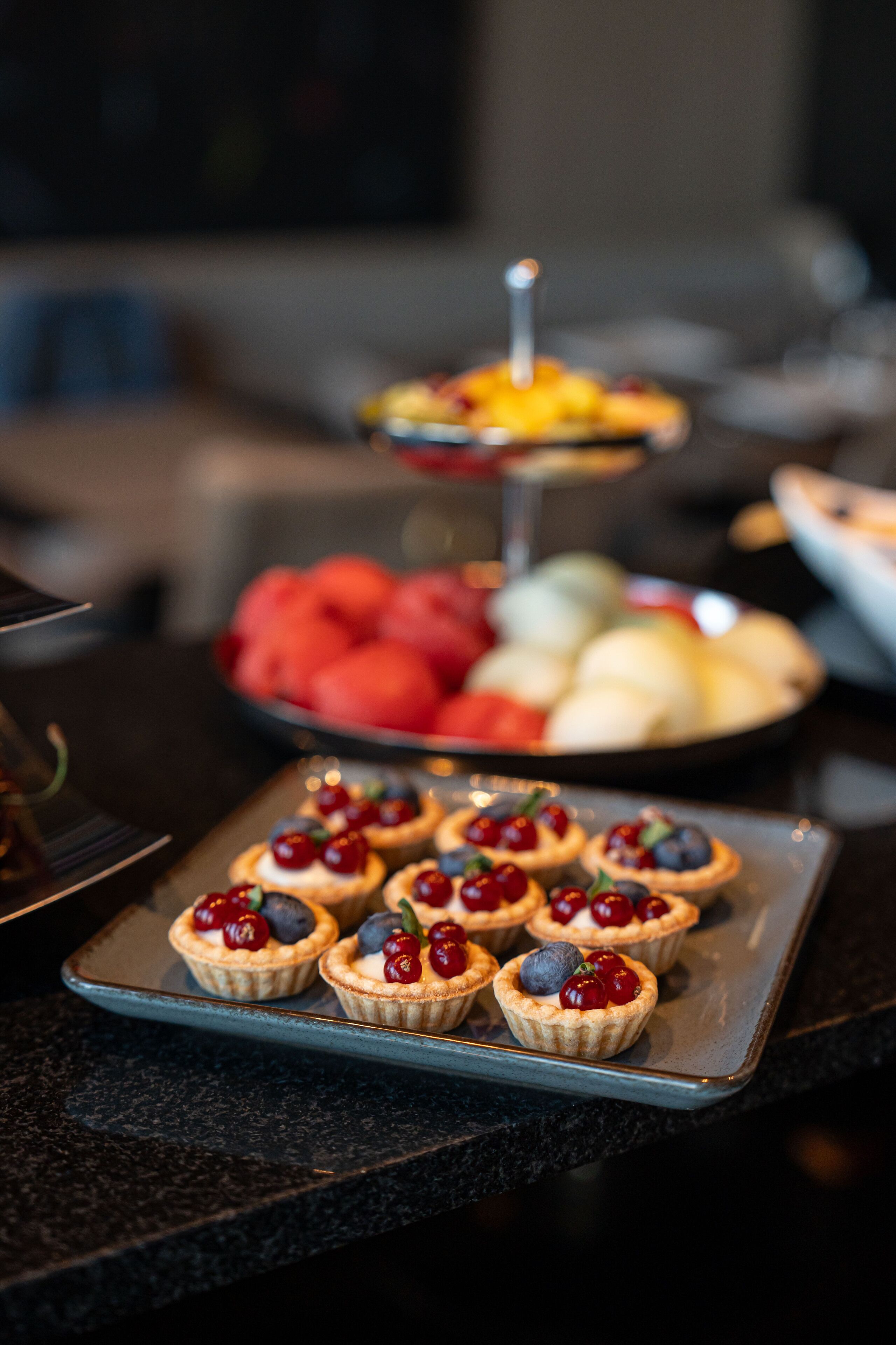 Une assiette remplie de petites tartes aux cerises et aux myrtilles, posée sur un plan de travail foncé.