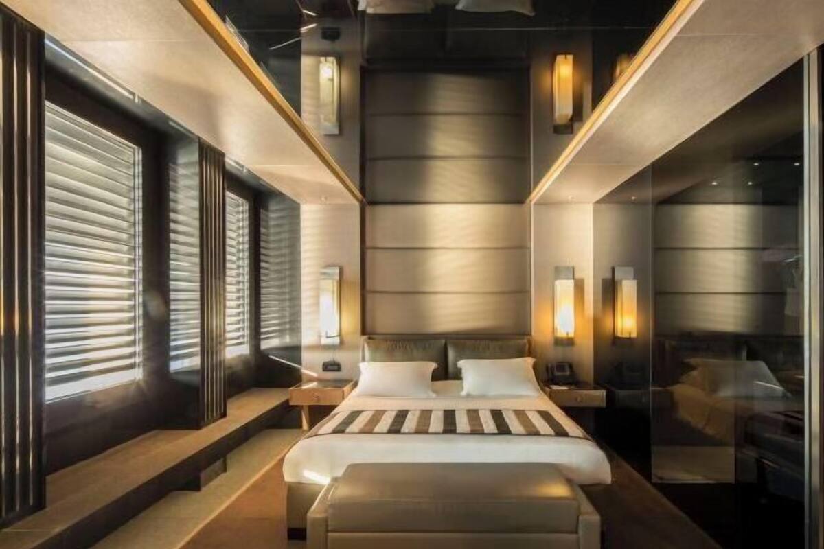 A modern hotel room with a large bed, bedside tables, a nightstand, and a glass partition.
