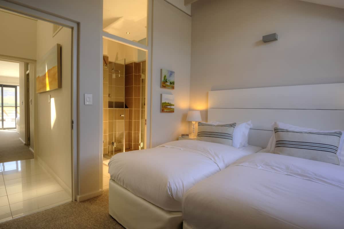 A hotel room with a large bed, a shower area, and a hallway leading to another room.