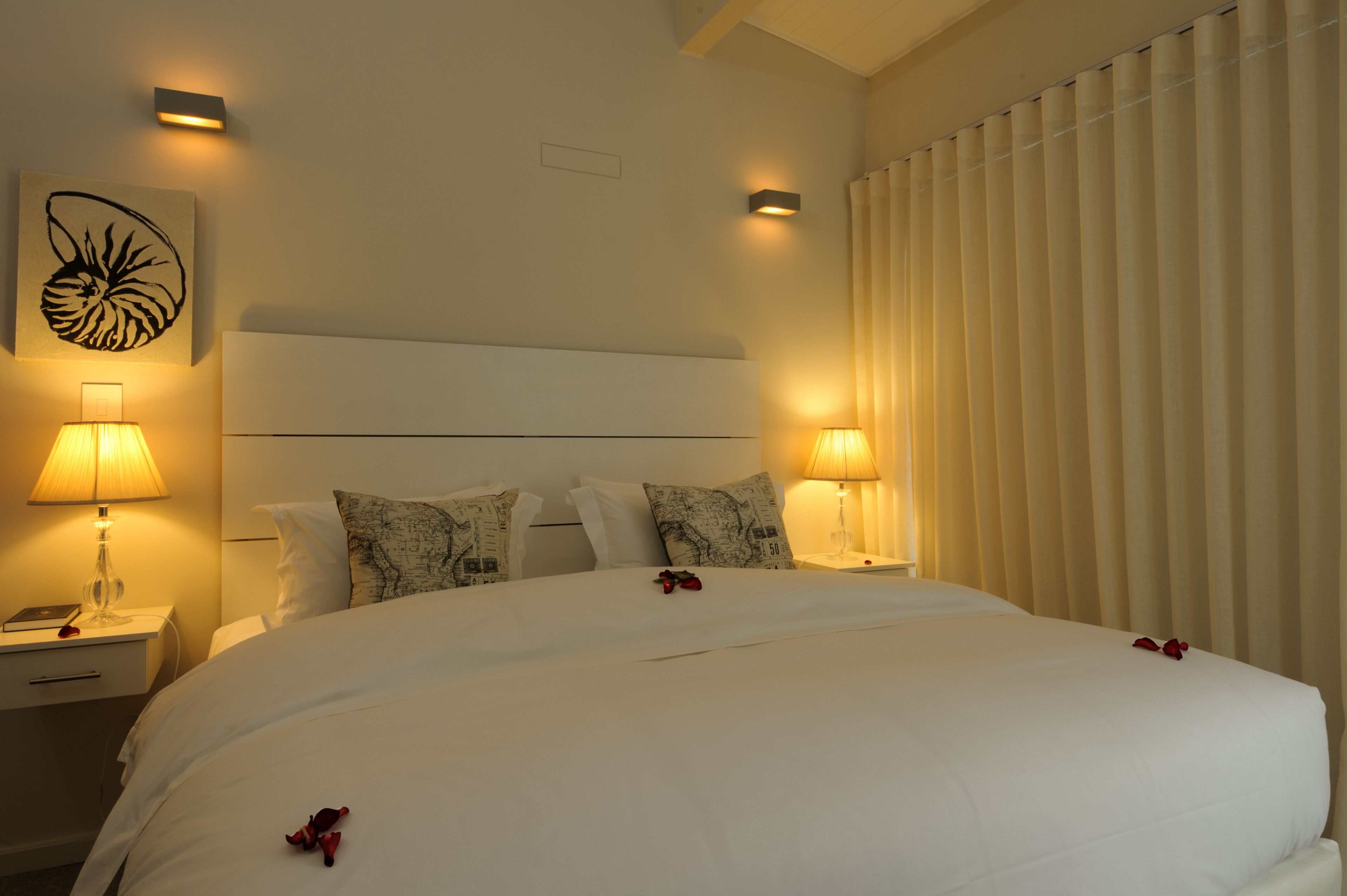 A hotel room with a large bed, two bedside tables with lamps, a headboard, and a wall-mounted artwork.