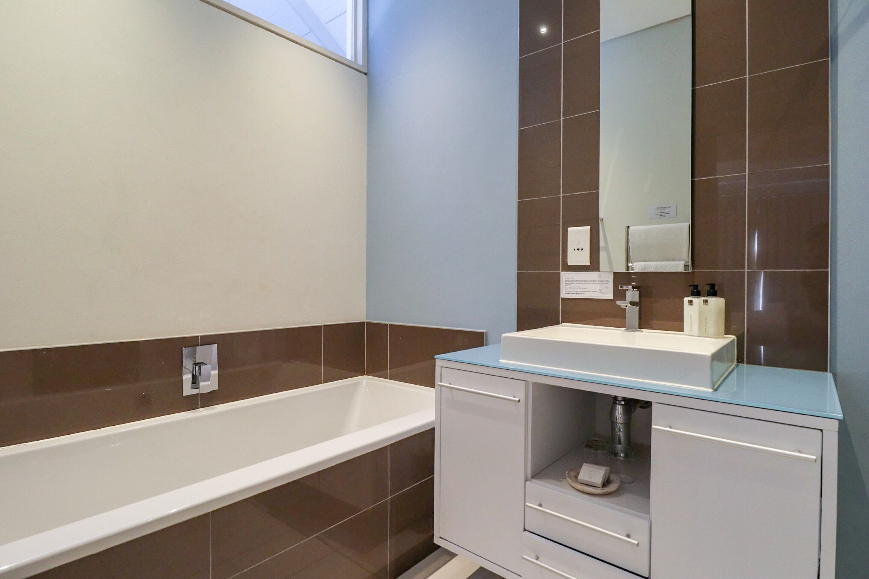 Une salle de bain moderne avec une baignoire, un meuble-lavabo avec un plateau en verre et un grand miroir.