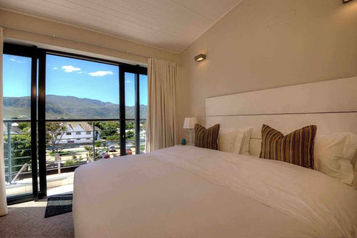 A hotel room with a large bed, a view of the mountains, and a balcony with a glass door.