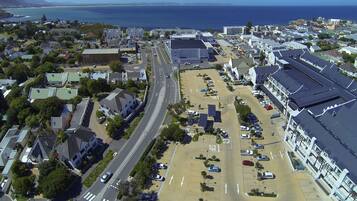 An aerial view of a coastal town with a parking lot, buildings, and a road leading to the sea.