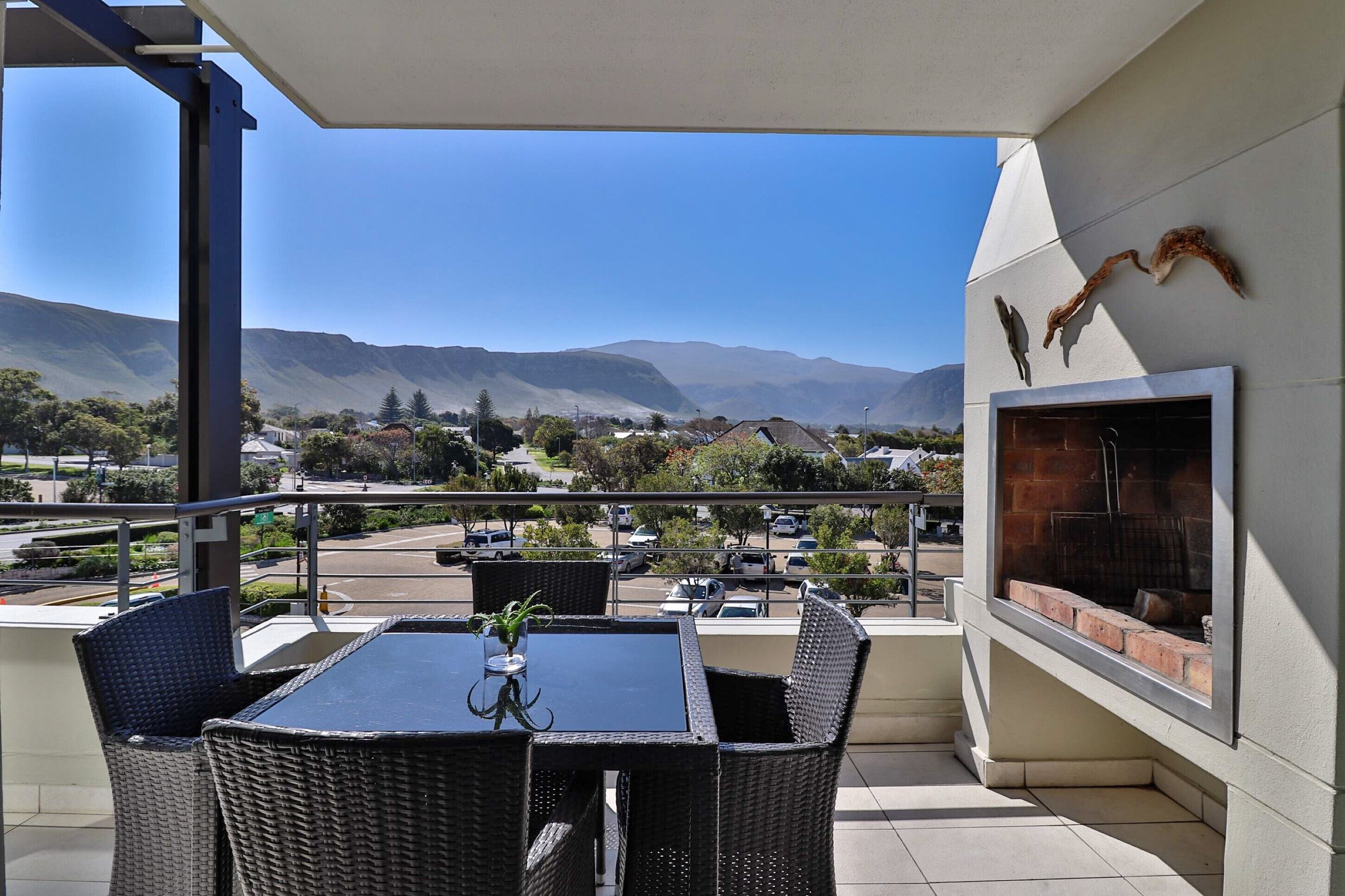 A balcony with wicker furniture, a grill, and a view of mountains and a parking lot.