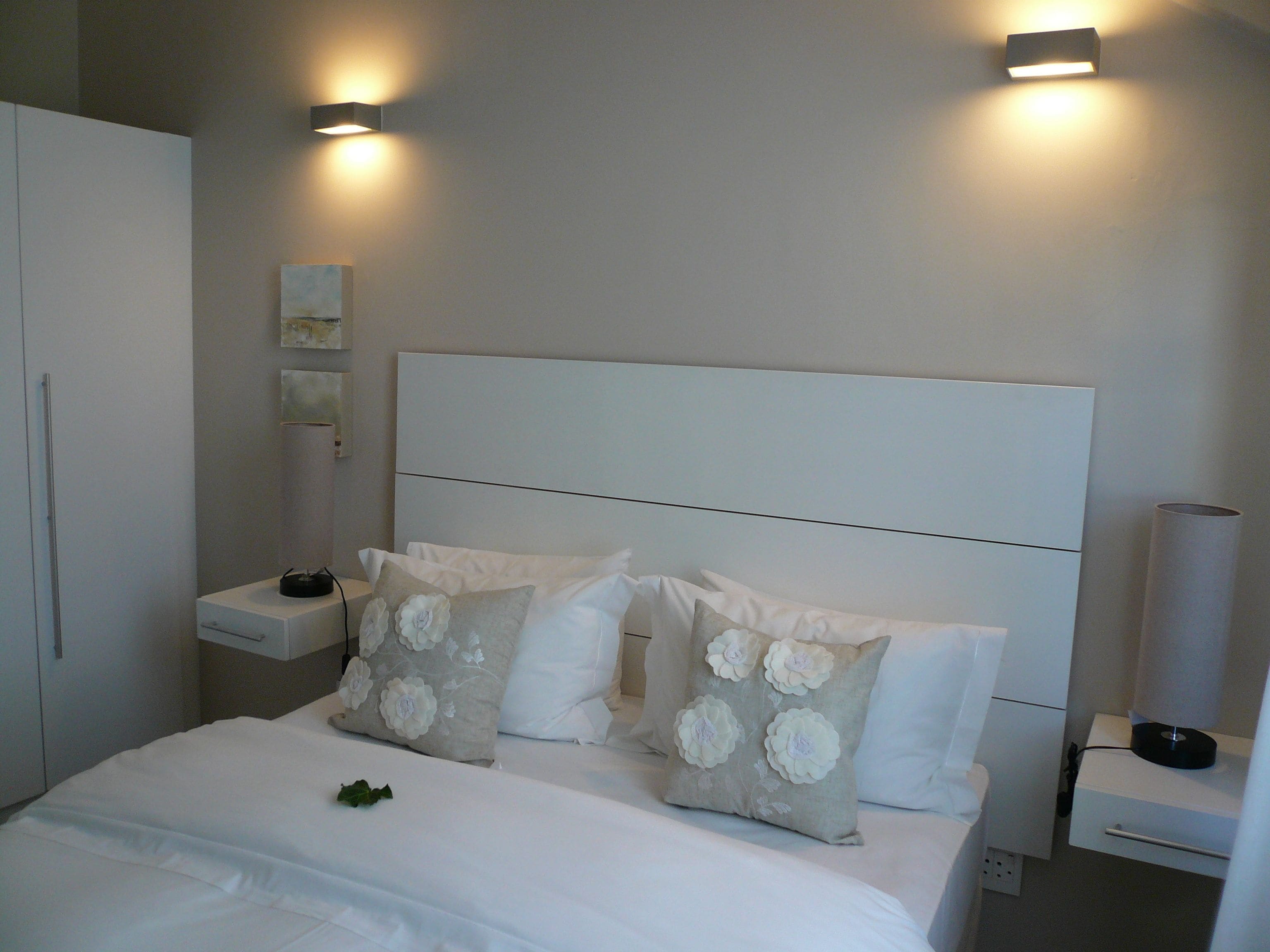 A modern bedroom with a large bed, two bedside tables, and wall-mounted lighting.