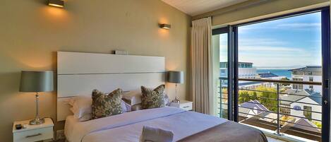 A hotel room with a large bed, two bedside lamps, a nightstand, and a view of buildings through a large window.