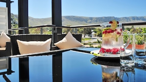 A table with a beverage pitcher and glasses, overlooking a mountainous landscape. - Whale Coast All Suite Hotel (Hermanus)