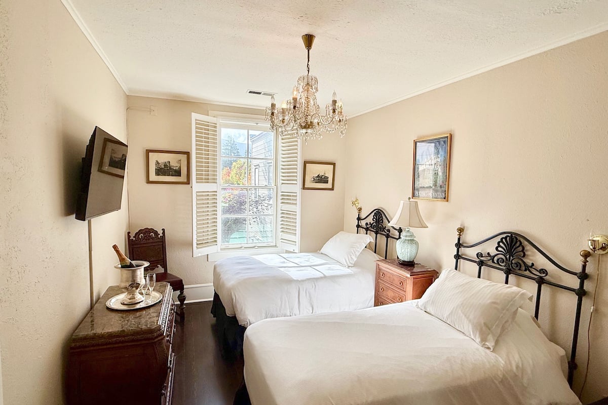 A bedroom with two beds, a chandelier, a dresser, and a television.