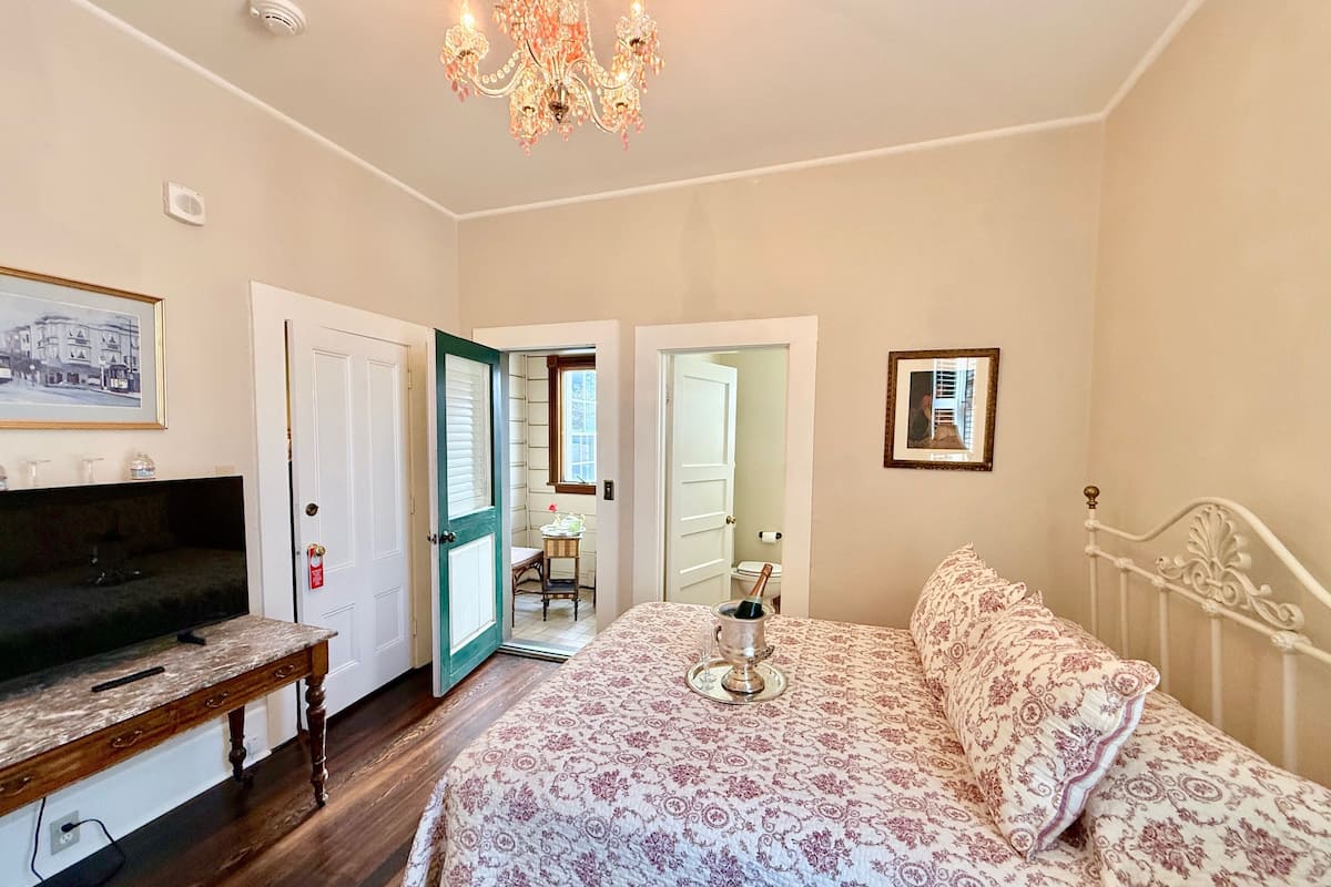 A bedroom with a bed, a television, a desk, and a chandelier.
