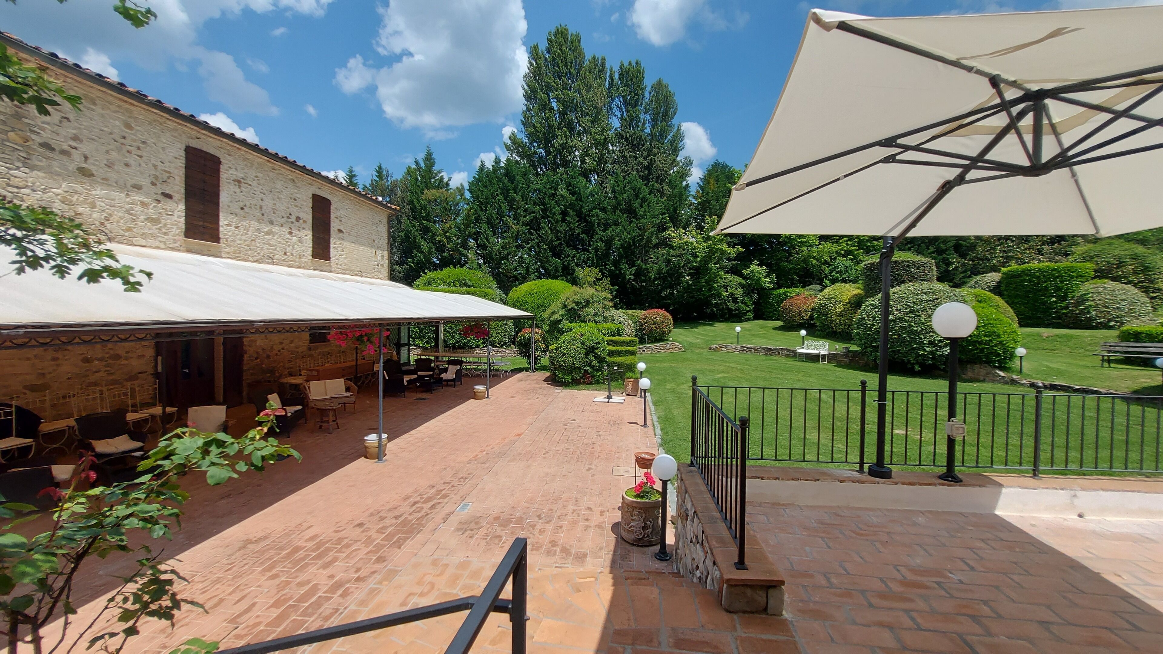 An outdoor patio with brick flooring, outdoor seating, and a large umbrella.