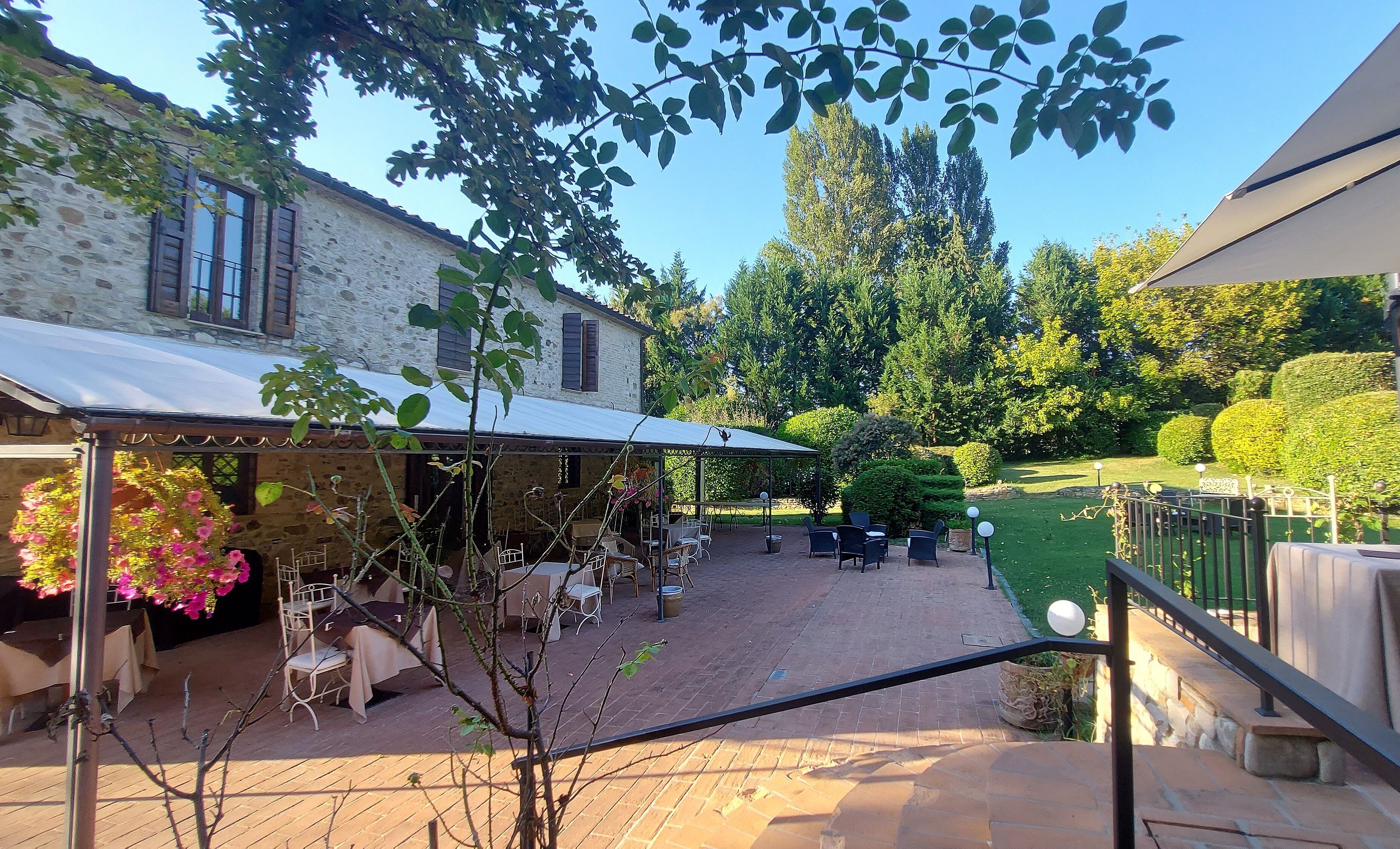 Un patio techado al aire libre con mesas y sillas, un edificio de piedra y un jardín bien cuidado.