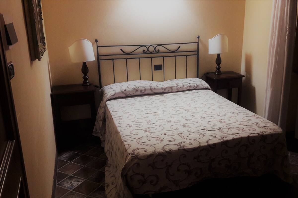 Un petit lit bien fait, recouvert d’une courtepointe à motifs floraux, avec deux lampes de chevet et une petite table placée à côté du lit.