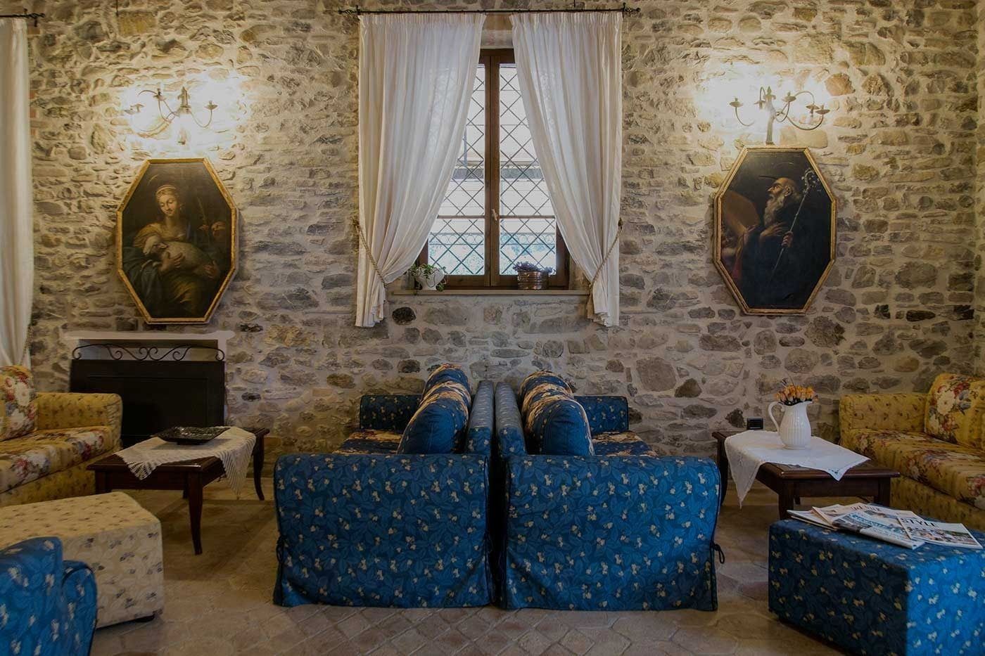 Una habitación con pared de piedra, dos sofás con tapicería floral, una chimenea y dos cuadros.