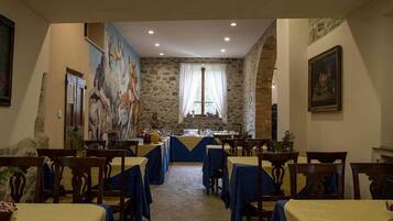 A dining area with stone walls, blue tablecloths, and wooden chairs.