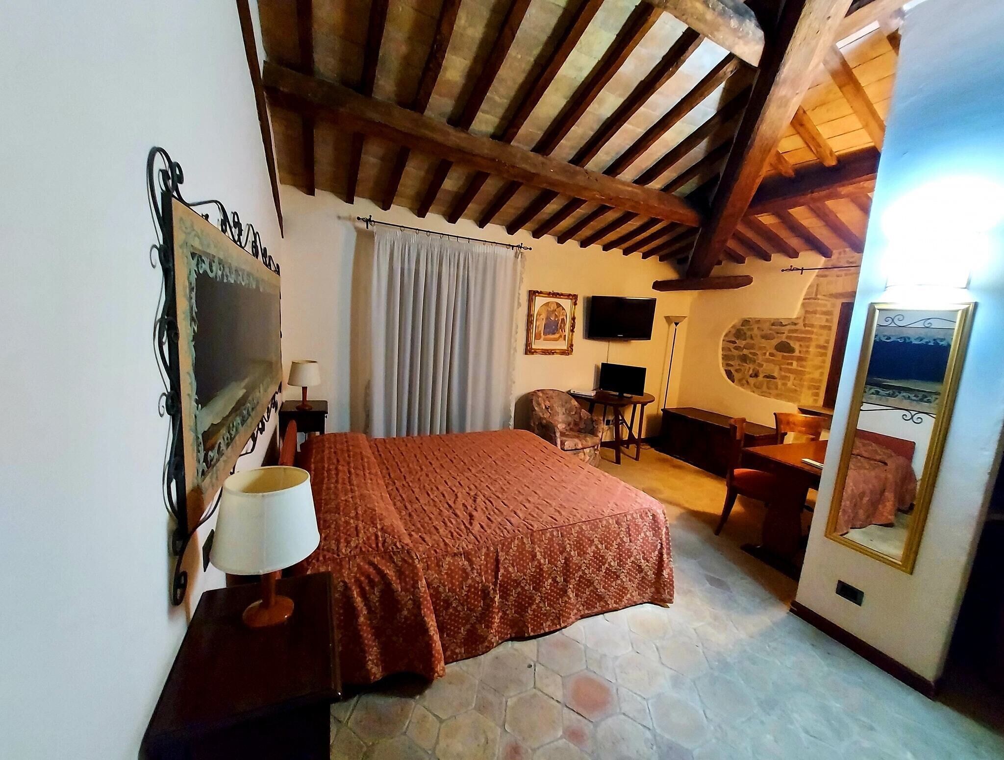 A bedroom with a large bed, a television, a stone wall, and a mirror.
