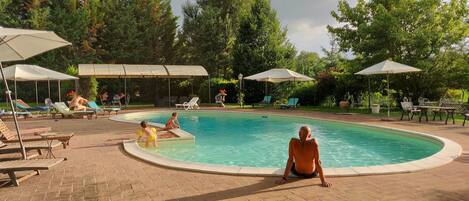 A pool area with lounge chairs and umbrellas, surrounded by trees.