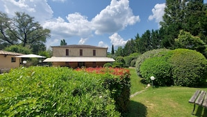 Un bâtiment en pierre, doté d’un toit en tuiles, entouré d’une végétation luxuriante et d’un jardin bien entretenu.