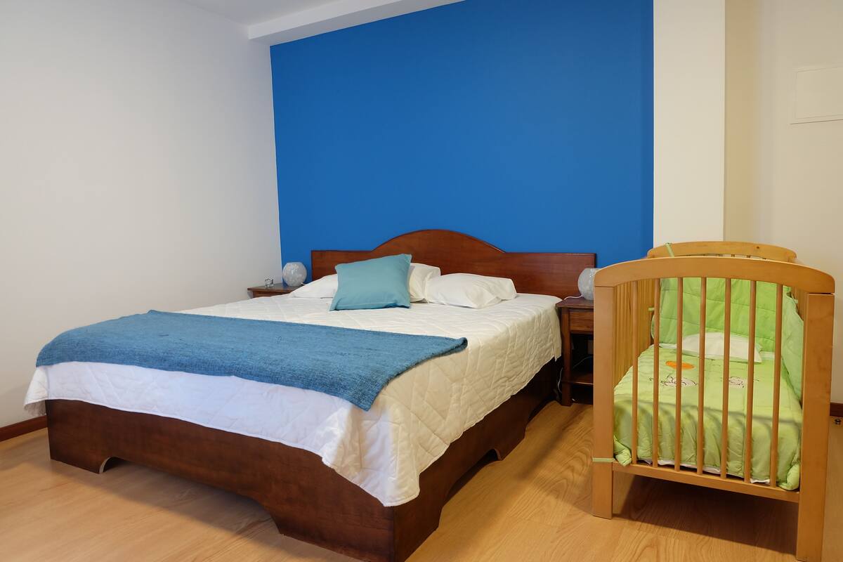 Quarto com cama de madeira, parede azul e berço.