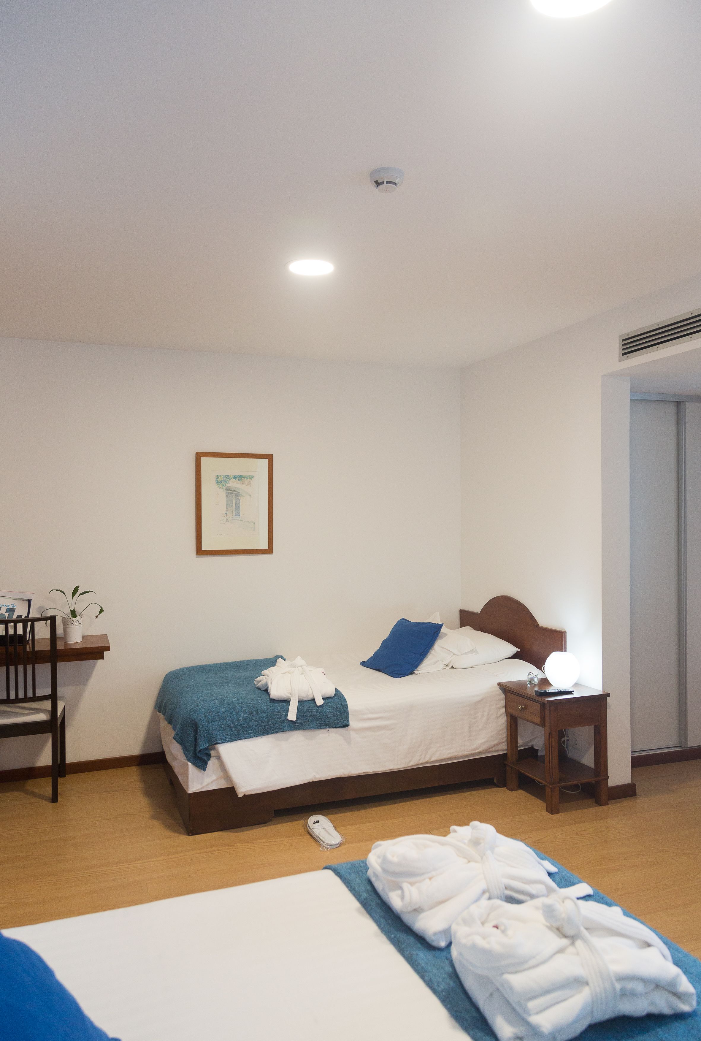 A hotel room with a bed, bedside table, and a desk with a chair.