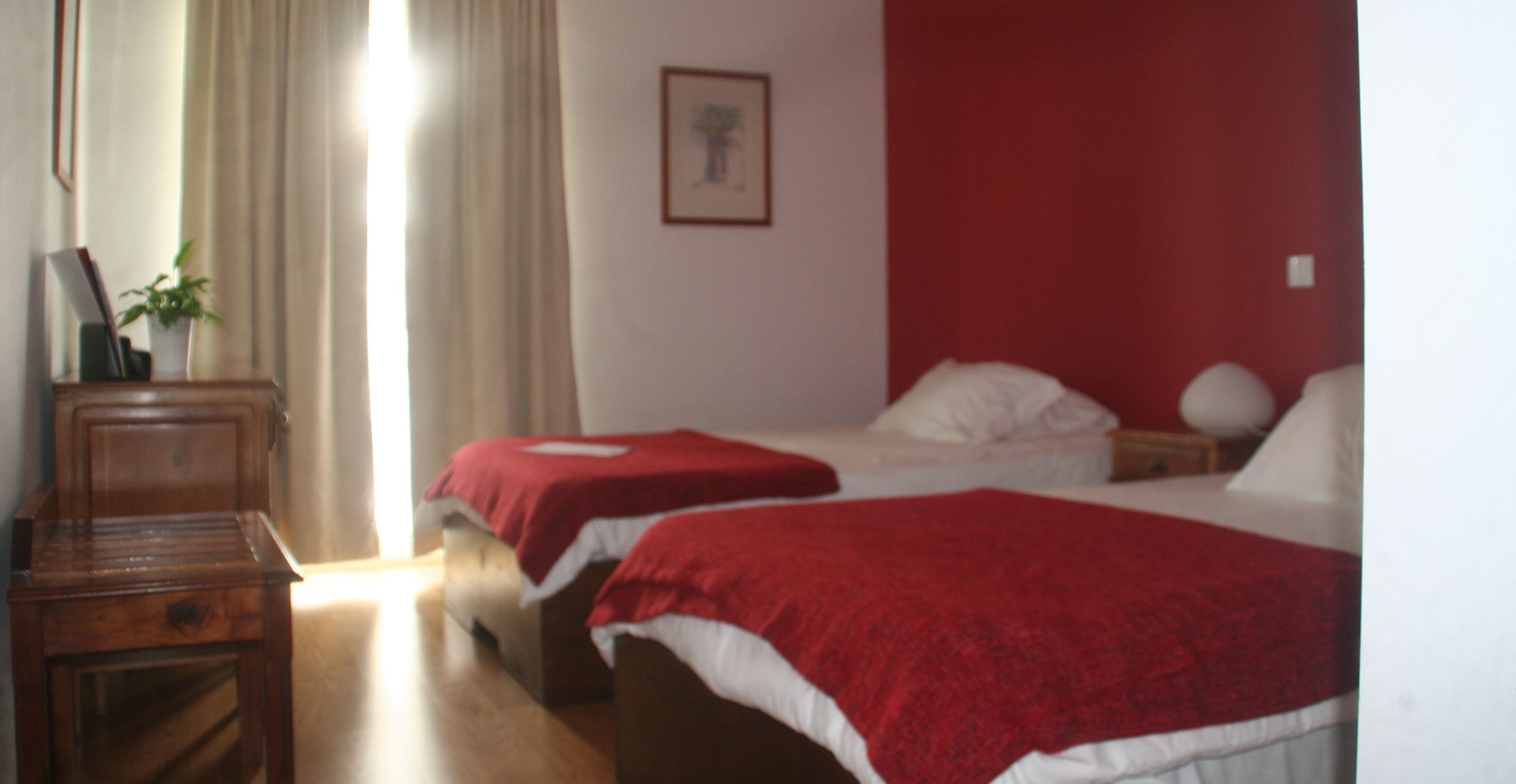 A hotel room with two beds, a wooden nightstand, a desk, and a potted plant.