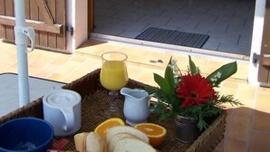 A breakfast setup with bread, orange slices, and a pitcher of juice on a table under an umbrella.