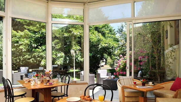 A sunlit dining area with large windows, wicker furniture, and a breakfast spread on a wooden table.