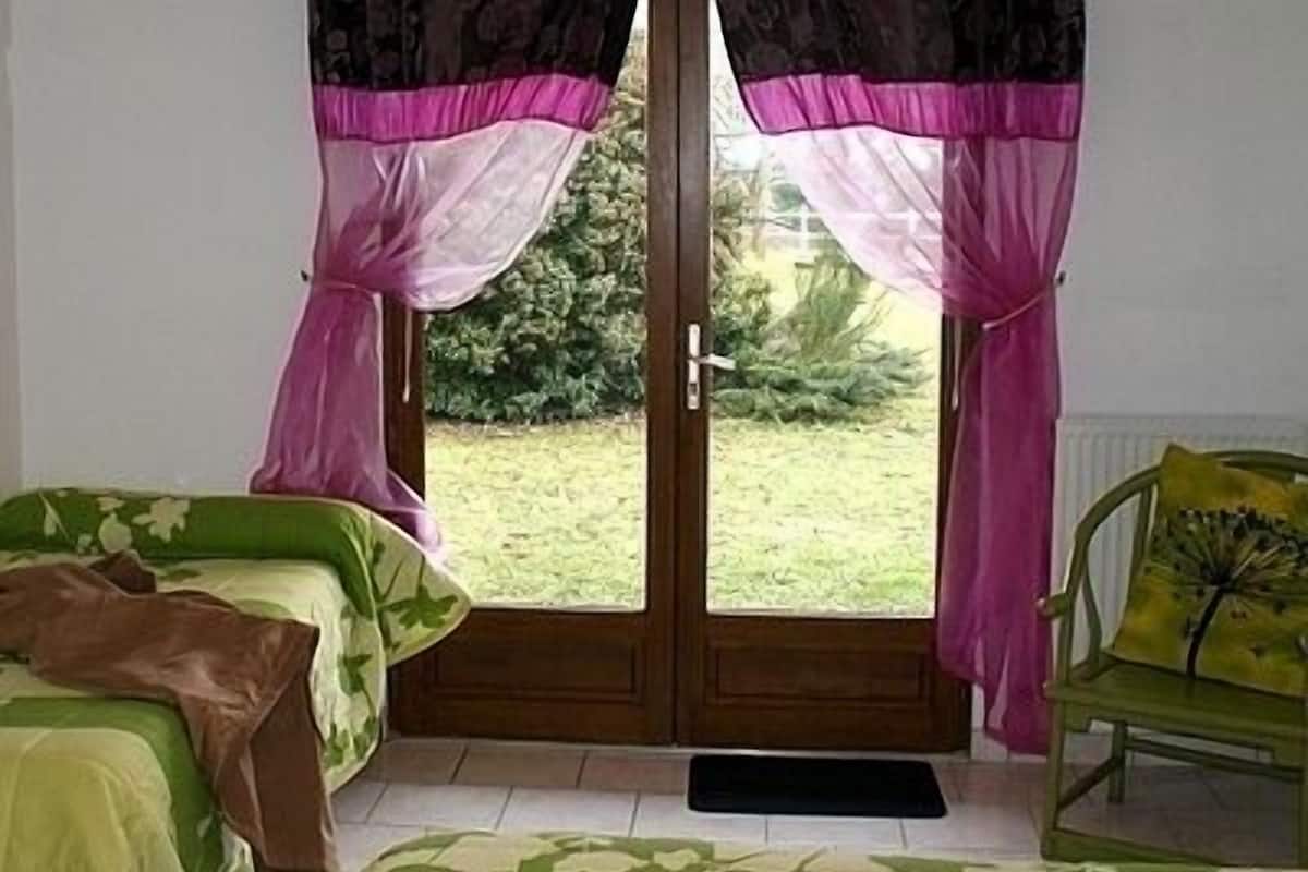 A room with two beds, a chair, and a door leading to a garden.