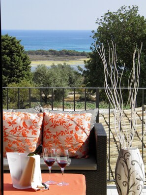 A balcony with a view of the sea, a table with wine glasses and a bottle, and a vase with branches. - Pantanelli di Vendicari (Noto)
