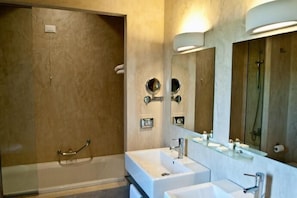Une salle de bain moderne avec une douche à l’italienne en verre, un grand miroir et deux lavabos.