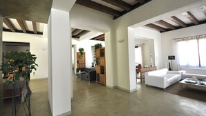 Un salón amplio con un sofá blanco, una mesa de centro y una estantería. Hay una planta en la esquina y piso de madera.