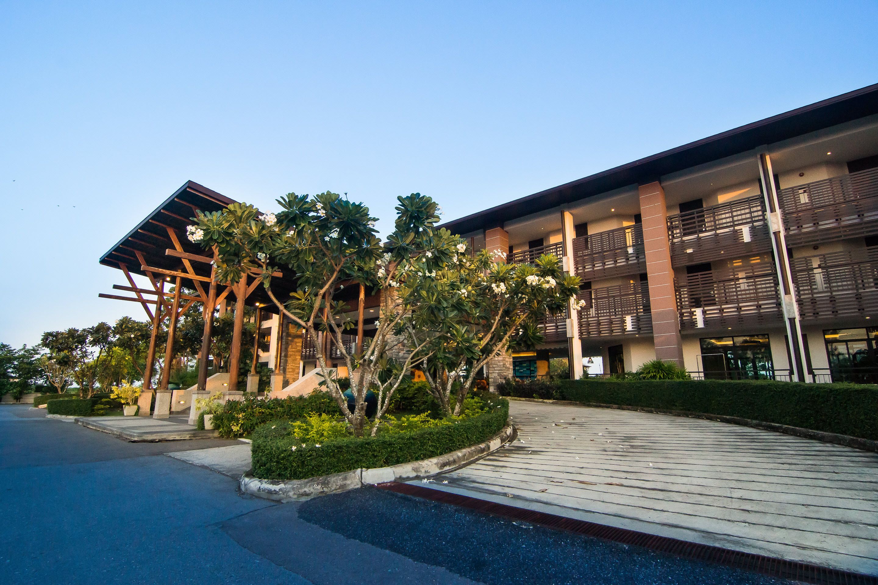 A modern building with a covered entrance, multiple balconies, and a landscaped area with trees and shrubs.