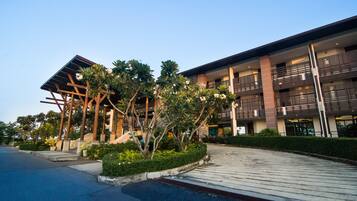 A modern building with a covered entrance, multiple balconies, and a landscaped area with trees and shrubs.