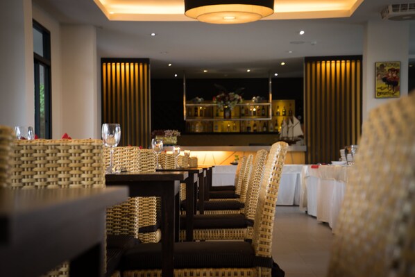 Un restaurante con sillas de mimbre, una mesa de madera oscura y una barra al fondo.