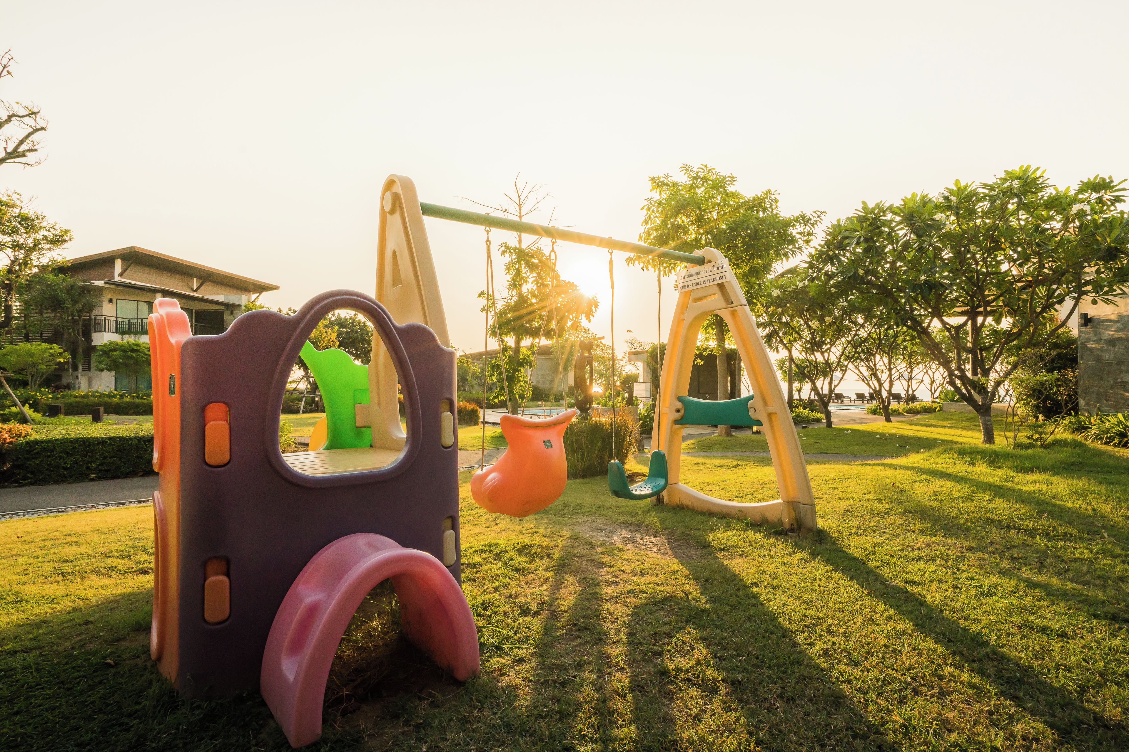 A playground with swings and a slide, surrounded by grass and trees.