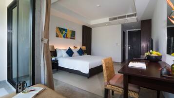 A modern hotel room with a large bed, a desk with a bowl of fruit, a chair, and a window with curtains.