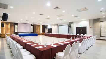 A conference room with a long table, white chairs, and a projector screen.