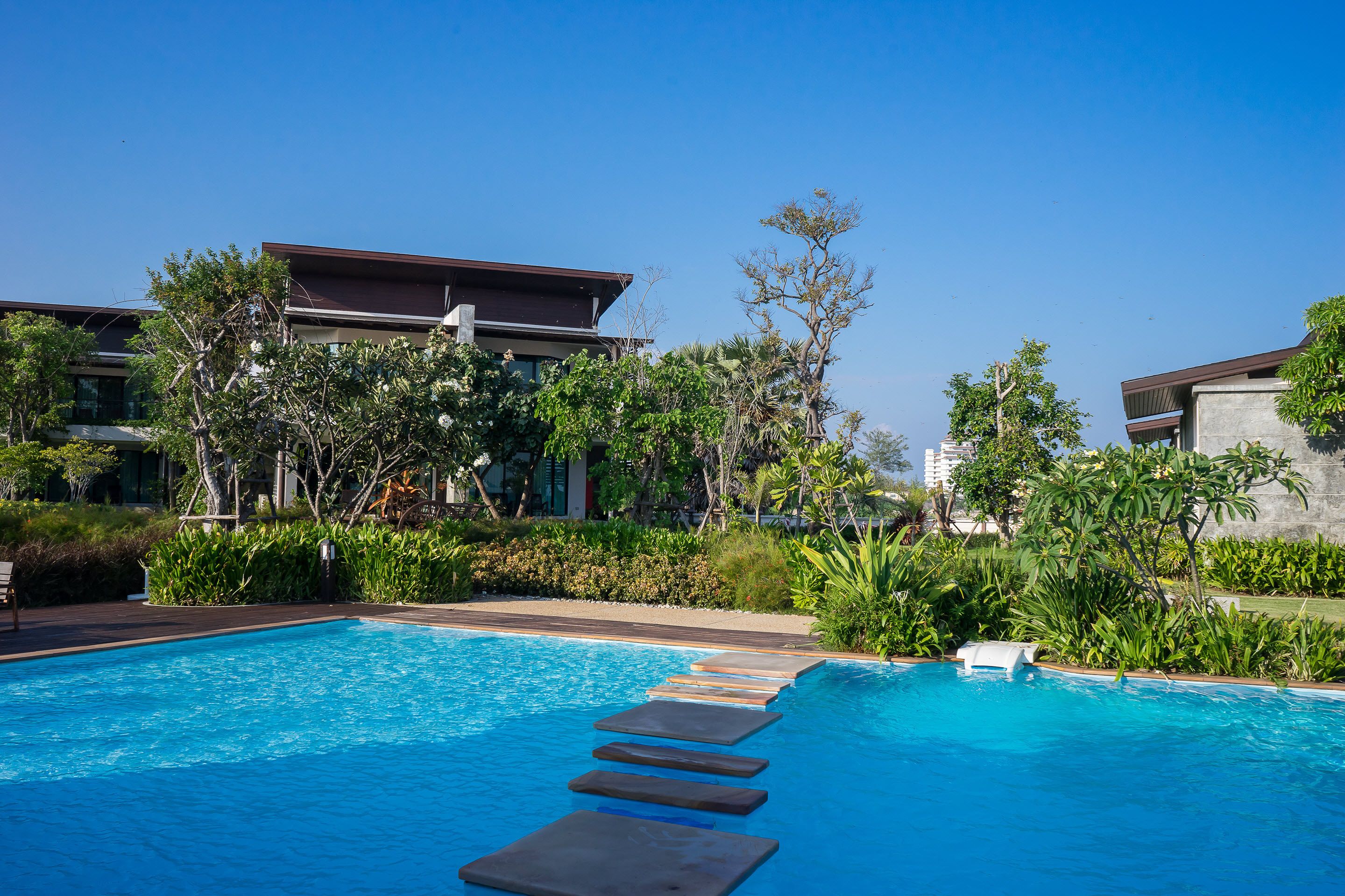 A swimming pool with stepping stones, surrounded by lush greenery and modern buildings.