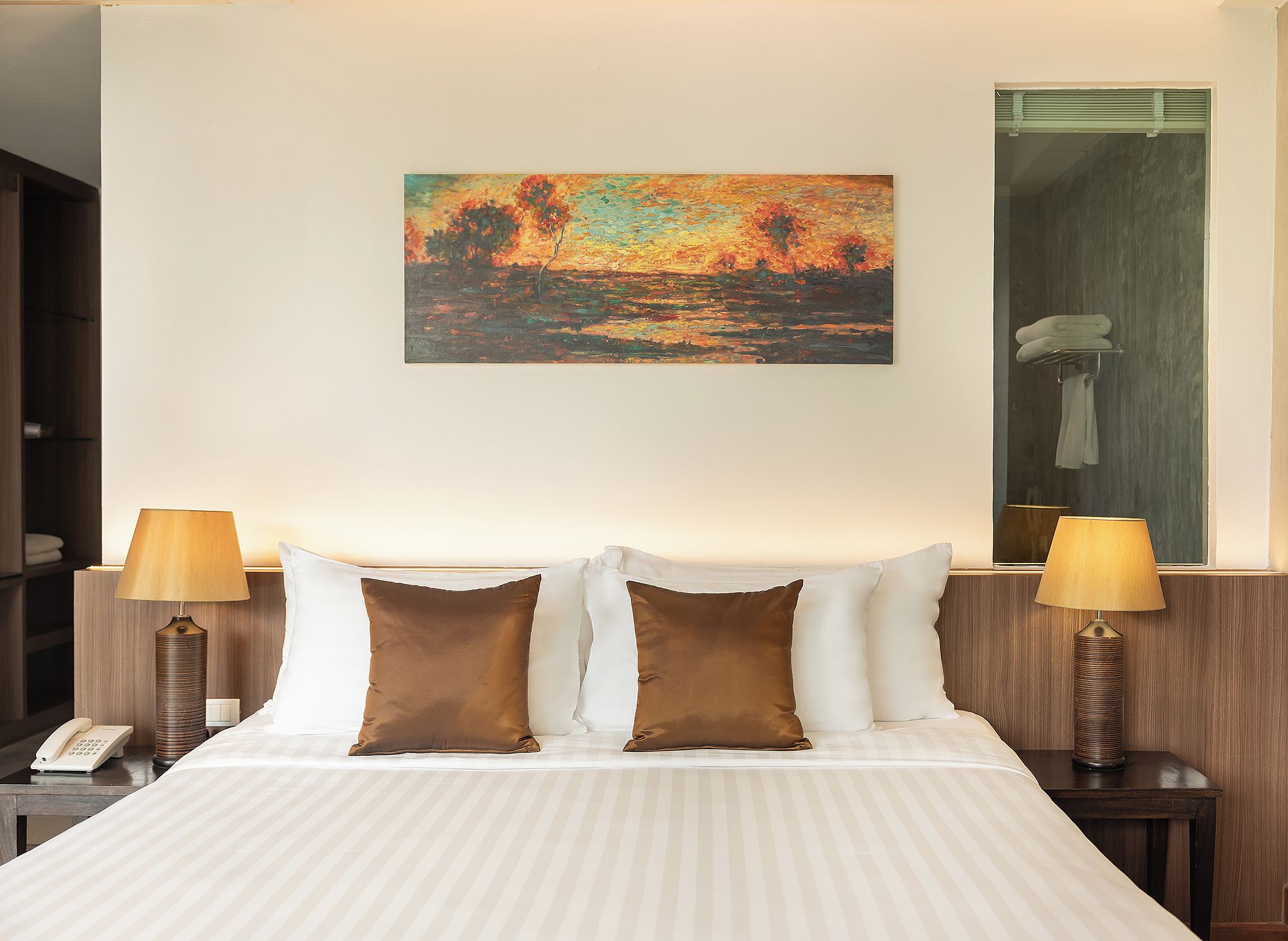Una habitación de hotel con una cama, dos lámparas de noche, un cuadro en la pared y un espejo sobre la cama.