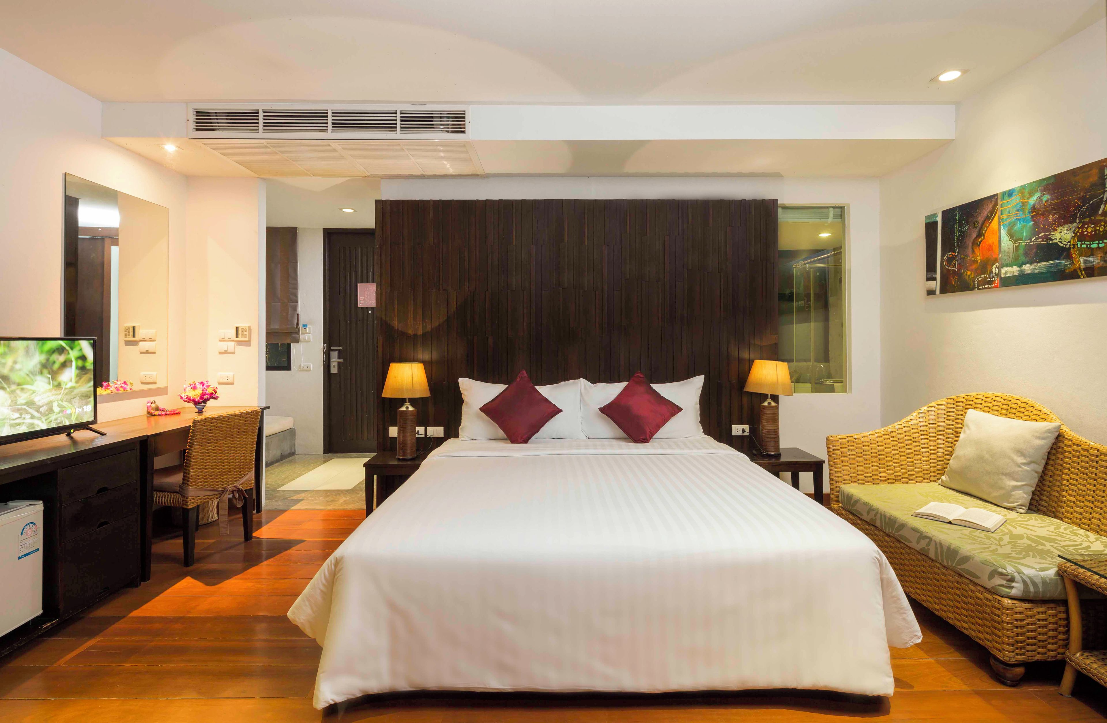 A hotel room with a large bed, a desk with a computer, a chair, a sofa, and a painting on the wall.