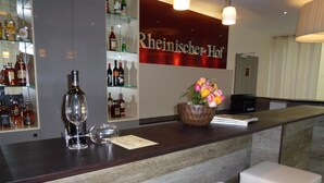 A bar area with a counter, glasses, and bottles of liquor. There are white cushioned stools and a decorative flower arrangement. - Milbor Hotel (Bad Soden am Taunus)